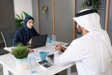المساواة بين المرأة والرجل، مفهوم التحاور وتبادل الأراء في خطط إنجاز الأعمال، إجراء مقابلة التعيين والتوظيف، رجل عربي خلجي إماراتي يرتدي الغترة والكندورة داخل المكتب يقوم بإجراء مقابلة عمل مع موظفة، مهن ووظائف إدارية مكتبية في الإمارات