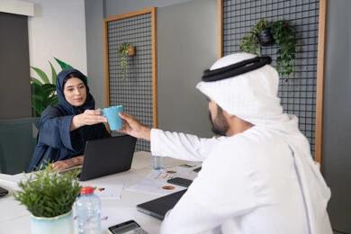 مفهوم التحاور وتبادل الأراء في خطط إنجاز الأعمال، إجراء مقابلة التعيين والتوظيف، رجل عربي خلجي إماراتي يرتدي الغترة والكندورة داخل المكتب يقوم بإجراء مقابلة عمل مع موظفة، مهن ووظائف إدارية مكتبية في الإمارات، المساواة بين المرأة والرجل