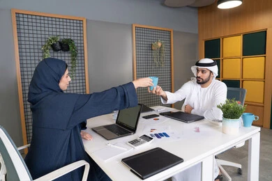 المساواة بين المرأة والرجل، مفهوم التحاور وتبادل الأراء في خطط إنجاز الأعمال، إجراء مقابلة التعيين والتوظيف، رجل عربي خلجي إماراتي يرتدي الغترة والكندورة داخل المكتب يقوم بإجراء مقابلة عمل مع موظفة، مهن ووظائف إدارية مكتبية في الإمارات