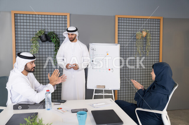 التعاون والتفاهم بين الزملاء ووضع الخطط الاستراتيجية لتحقيق الأهداف، استخدام السبورة لضمان فهم واضح وشامل للاعمال، عقد اجتماع داخل مقر الشركة، مجموعة من الموظفين العرب الخليجيين الاماراتيين يتعلمون اساليب العمل والتطوير المهني، روح الفريق الواحد والعمل الجماعي
