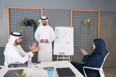 Collaboration and understanding among colleagues, developing strategic plans to achieve goals, using the whiteboard to ensure a clear and comprehensive understanding of the business, holding a meeting at the company's headquarters, a group of Arab Gulf Emirati employees learning work methods and professional development, team spirit and teamwork.