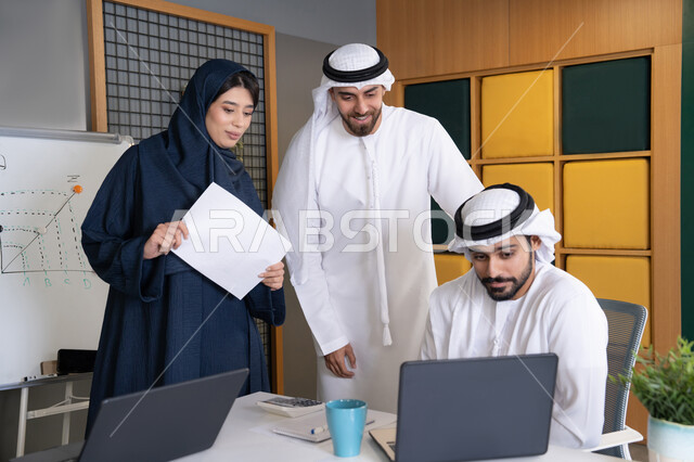 Problem solving and data analysis, business meeting and discussion at company headquarters, an Emirati Gulf Arab businessman wearing a kandura and ghutra working on a laptop with his colleagues inside the office, studying and developing new projects in UAE companies, using a modern technical device
