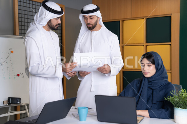 Work environment in UAE companies, using modern technology, achieving company goals, meeting and discussing work at company headquarters, an Emirati Gulf Arab businesswoman wearing a hijab and abaya working on a laptop with her colleagues inside the office, studying and developing new projects