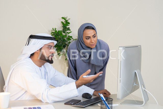 Using a computer, understanding and cooperation between colleagues and developing strategic plans, holding a meeting at the company headquarters, two Arab Gulf Emirati employees learning work methods and professional development, exchanging experiences and information to achieve goals, team spirit and teamwork