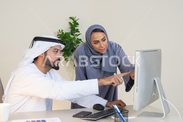 الاشارة باصبع السبابة الى شاشة الحاسوب، تبادل الخبرات والمعلومات لتحقيق الاهداف، روح الفريق الواحد والعمل الجماعي، التفاهم والتعاون بين الزملاء ووضع الخطط الاستراتيجية، عقد اجتماع داخل مقر الشركة، موظفان عربيان خليجيان اماراتيان يتعلمان اساليب العمل والتطوير المهني