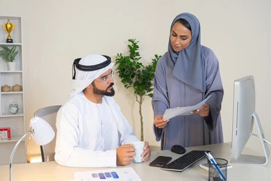 Discussion and understanding between employees, exchange of experiences and information to achieve goals, team spirit and teamwork, understanding and cooperation between colleagues and development of strategic plans, holding a meeting at the company headquarters, two Arab Gulf Emirati employees learning work methods and professional development