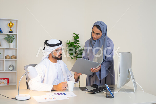 Team spirit and teamwork, understanding and cooperation among colleagues and developing strategic plans, holding a meeting at the company headquarters, two Arab Gulf Emirati employees learning work methods and professional development, discussion and understanding among employees, exchanging experiences and information to achieve goals