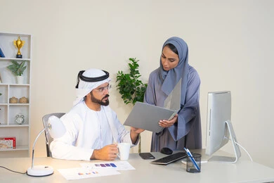 Team spirit and teamwork, understanding and cooperation among colleagues and developing strategic plans, holding a meeting at the company headquarters, two Arab Gulf Emirati employees learning work methods and professional development, discussion and understanding among employees, exchanging experiences and information to achieve goals