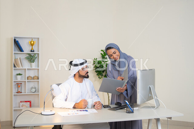 Team spirit and teamwork, understanding and cooperation among colleagues and developing strategic plans, holding a meeting at the company headquarters, two Arab Gulf Emirati employees learning work methods and professional development, discussion and understanding among employees, exchanging experiences and information to achieve goals
