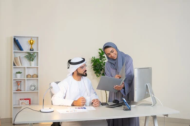 Team spirit and teamwork, understanding and cooperation among colleagues and developing strategic plans, holding a meeting at the company headquarters, two Arab Gulf Emirati employees learning work methods and professional development, discussion and understanding among employees, exchanging experiences and information to achieve goals