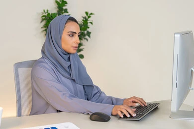 ادارة الأعمال وانجاز المهام المطلوبة، الكتابة على لوحة المفاتيح، مهنة ووظيفة نسائية،  إمرأة عربية خليجية اماراتية محجبة ترتدي عباءة ملونة تجلس خلف الطاولة، سيدة سعودية تستخدم الحاسوب في المكتب، استخدام جهاز تقني حديث ومتطور، ايماءات التركيز والاندماج