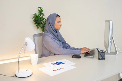 الكتابة على لوحة المفاتيح، مهنة ووظيفة نسائية،  إمرأة عربية خليجية اماراتية محجبة ترتدي عباءة ملونة تجلس خلف الطاولة، سيدة سعودية تستخدم الحاسوب في المكتب، استخدام جهاز تقني حديث ومتطور، ايماءات التركيز والاندماج، ادارة الأعمال وانجاز المهام المطلوبة