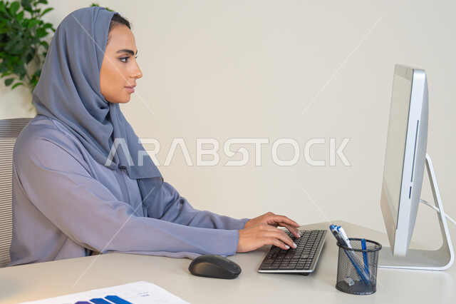 الكتابة على لوحة المفاتيح، مهنة ووظيفة نسائية،  إمرأة عربية خليجية اماراتية محجبة ترتدي عباءة ملونة تجلس خلف الطاولة، سيدة سعودية تستخدم الحاسوب في المكتب، استخدام جهاز تقني حديث ومتطور، ايماءات التركيز والاندماج، ادارة الأعمال وانجاز المهام المطلوبة