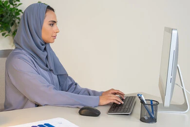 الكتابة على لوحة المفاتيح، مهنة ووظيفة نسائية،  إمرأة عربية خليجية اماراتية محجبة ترتدي عباءة ملونة تجلس خلف الطاولة، سيدة سعودية تستخدم الحاسوب في المكتب، استخدام جهاز تقني حديث ومتطور، ايماءات التركيز والاندماج، ادارة الأعمال وانجاز المهام المطلوبة