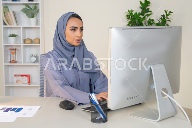 الكتابة على لوحة المفاتيح، مهنة ووظيفة نسائية،  إمرأة عربية خليجية اماراتية محجبة ترتدي عباءة ملونة تجلس خلف الطاولة، سيدة سعودية تستخدم الحاسوب في المكتب، استخدام جهاز تقني حديث ومتطور، ايماءات التركيز والاندماج، ادارة الأعمال وانجاز المهام المطلوبة