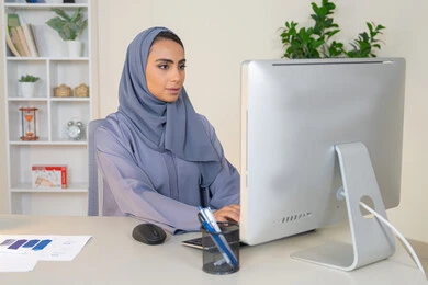 الكتابة على لوحة المفاتيح، مهنة ووظيفة نسائية،  إمرأة عربية خليجية اماراتية محجبة ترتدي عباءة ملونة تجلس خلف الطاولة، سيدة سعودية تستخدم الحاسوب في المكتب، استخدام جهاز تقني حديث ومتطور، ايماءات التركيز والاندماج، ادارة الأعمال وانجاز المهام المطلوبة