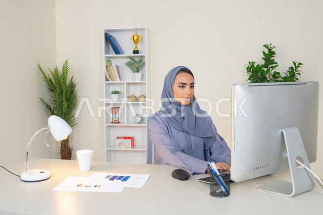 الكتابة على لوحة المفاتيح، مهنة ووظيفة نسائية،  إمرأة عربية خليجية اماراتية محجبة ترتدي عباءة ملونة تجلس خلف الطاولة، سيدة سعودية تستخدم الحاسوب في المكتب، استخدام جهاز تقني حديث ومتطور، ايماءات التركيز والاندماج، ادارة الأعمال وانجاز المهام المطلوبة