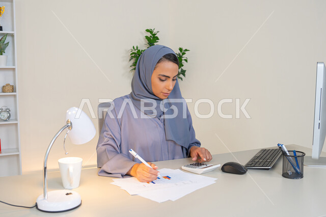 Office job in a Gulf company, analyzing statistical data results, a veiled Emirati Gulf Arab woman wearing an abaya sitting behind a desk working on a computer to complete tasks in the office, a Saudi woman taking notes on paper, using a calculator to perform mathematical operations