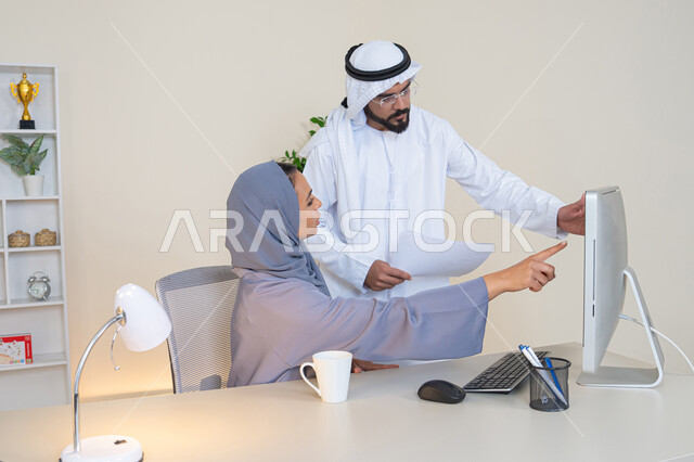 الاشارة باصبع السبابة الى شاشة الحاسوب، تبادل الخبرات والمعلومات لتحقيق الاهداف، روح الفريق الواحد والعمل الجماعي، التفاهم والتعاون بين الزملاء ووضع الخطط الاستراتيجية، عقد اجتماع داخل مقر الشركة، موظفان عربيان خليجيان اماراتيان يتعلمان اساليب العمل والتطوير المهني