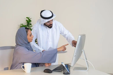 الاشارة باصبع السبابة الى شاشة الحاسوب، تبادل الخبرات والمعلومات لتحقيق الاهداف، روح الفريق الواحد والعمل الجماعي، التفاهم والتعاون بين الزملاء ووضع الخطط الاستراتيجية، عقد اجتماع داخل مقر الشركة، موظفان عربيان خليجيان اماراتيان يتعلمان اساليب العمل والتطوير المهني