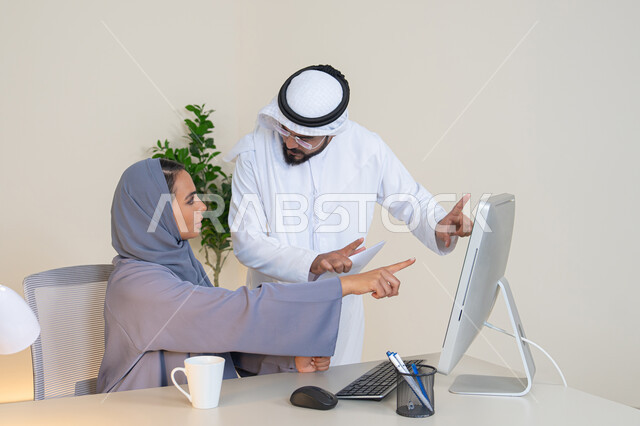Pointing the index finger at the computer screen, exchanging experiences and information to achieve goals, team spirit and teamwork, understanding and cooperation between colleagues and developing strategic plans, holding a meeting at the company headquarters, two Arab Gulf Emirati employees learning work methods and professional development
