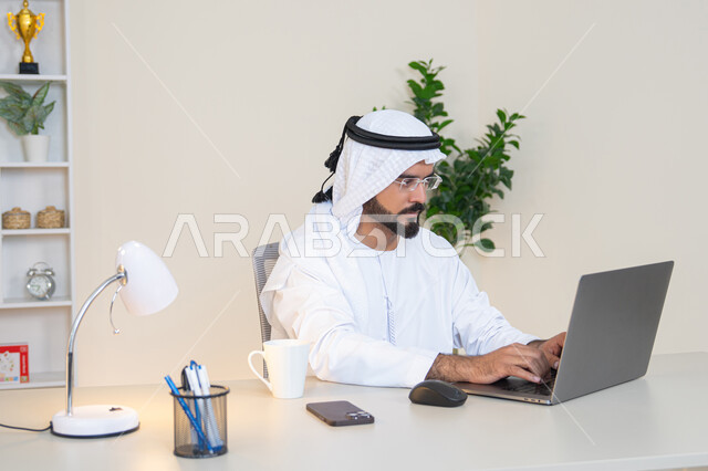 تطور الشركات الاماراتية، إتمام مهام العمل في المكتب، إدارة شؤون الأعمال وتنظيمها، احتساء مشروب القهوة، استخدام جهاز تقني حديث ومتطور، رجل عربي خليجي اماراتي يرتدي الكندورة والغترة البيضاء يستخدم الحاسوب، مهنة ووظيفة مكتبية، دمج العمل مع التقنية والتكنولوجيا