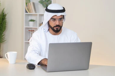 تطور الشركات الاماراتية، إتمام مهام العمل في المكتب، إدارة شؤون الأعمال وتنظيمها، احتساء مشروب القهوة، استخدام جهاز تقني حديث ومتطور، رجل عربي خليجي اماراتي يرتدي الكندورة والغترة البيضاء يستخدم الحاسوب، مهنة ووظيفة مكتبية، دمج العمل مع التقنية والتكنولوجيا