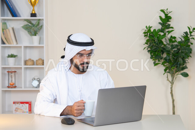 تطور الشركات الاماراتية، إتمام مهام العمل في المكتب، إدارة شؤون الأعمال وتنظيمها، احتساء مشروب القهوة، استخدام جهاز تقني حديث ومتطور، رجل عربي خليجي اماراتي يرتدي الكندورة والغترة البيضاء يستخدم الحاسوب، مهنة ووظيفة مكتبية، دمج العمل مع التقنية والتكنولوجيا