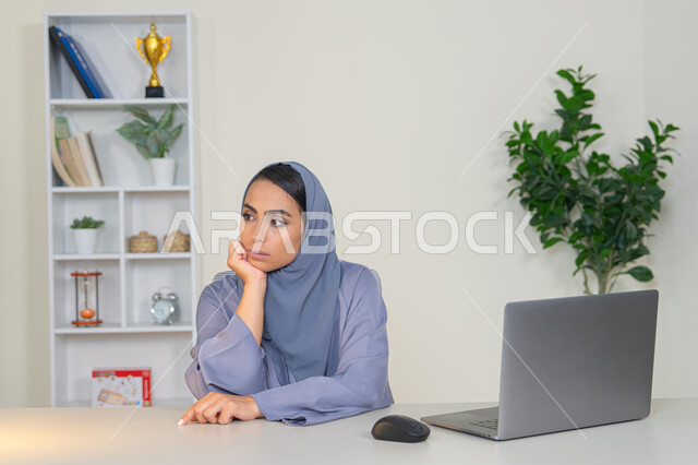 Working in a Gulf company, feeling bored, an Emirati woman using modern advanced technology in the office, a veiled Saudi Arabian Gulf woman wearing an abaya sitting behind a table with boredom, trying to find a solution to a problem, absent-mindedness and thinking, an office profession and job