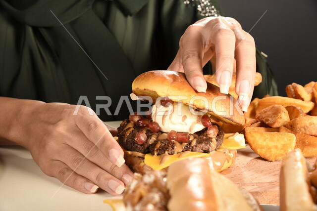 Burger sandwich with layers of meat and lettuce with melted cheese, a Saudi Arabian Gulf woman eating a burger, enjoying eating a burger, fast food, the harms of eating a lot of fast food