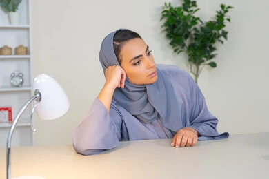 A veiled Saudi Arabian Gulf woman wearing an abaya sitting behind a desk in the office with bored gestures, an Emirati woman trying to find a solution to a problem, absent-mindedness and thinking, an office job and profession, working in Gulf companies, feeling bored and fed up