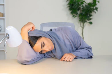 Feeling bored, a veiled Saudi Arabian Gulf woman wearing an abaya sitting behind a desk in the office with boredom gestures, an Emirati woman trying to find a solution to a problem, absent-mindedness and thinking, an office job and profession, working in Gulf companies