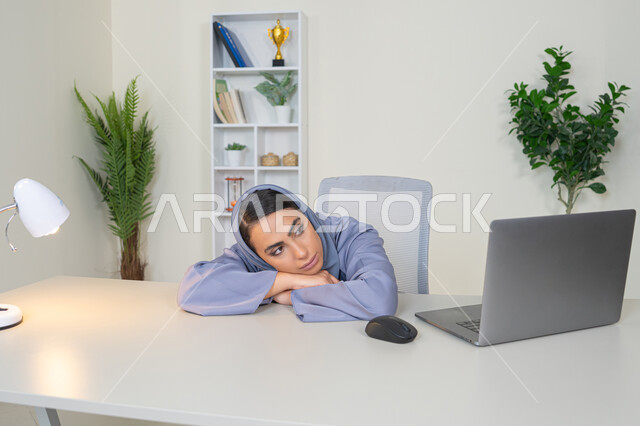 A veiled Saudi Arabian Gulf woman wearing an abaya sitting behind a table with bored gestures, trying to find a solution to a problem, absent-minded and thinking, an office job and profession, working in Gulf companies, feeling bored and fed up, an Emirati woman using modern advanced technology in the office