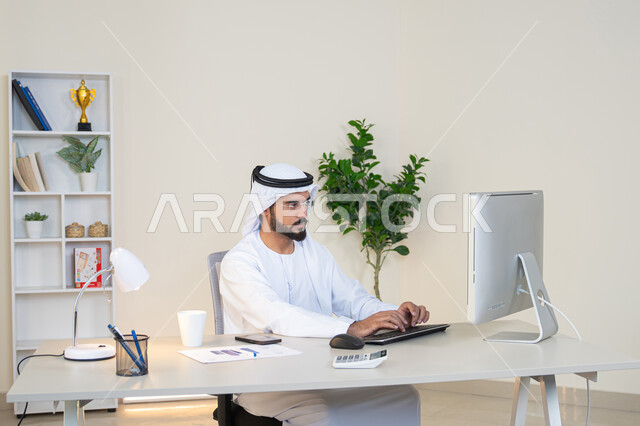 تطور الشركات الاماراتية، إتمام مهام العمل في المكتب، إدارة شؤون الأعمال وتنظيمها، احتساء مشروب القهوة، استخدام جهاز تقني حديث ومتطور، رجل عربي خليجي اماراتي يرتدي الكندورة والغترة البيضاء يستخدم الحاسوب، مهنة ووظيفة مكتبية، دمج العمل مع التقنية والتكنولوجيا