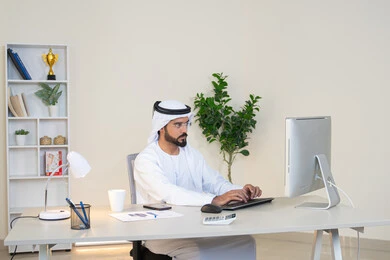 تطور الشركات الاماراتية، إتمام مهام العمل في المكتب، إدارة شؤون الأعمال وتنظيمها، احتساء مشروب القهوة، استخدام جهاز تقني حديث ومتطور، رجل عربي خليجي اماراتي يرتدي الكندورة والغترة البيضاء يستخدم الحاسوب، مهنة ووظيفة مكتبية، دمج العمل مع التقنية والتكنولوجيا