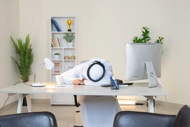 النوم على طاولة العمل، ايماءات النعاس والتعب والإرهاق، رجل عربي خليجي اماراتي يرتدي الكندورة والغترة البيضاء يجلس خلف الطاولة في المكتب ويقوم بأخذ قسط من الراحة، العمل في شركات الامارات العربية المتحدة، مهنة ووظيفة مكتبية