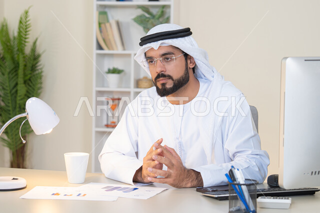 Accomplishing tasks, managing and organizing business affairs, listening to someone, an Arab Gulf Emirati man wearing a white kandura and ghutra sitting behind a table drinking coffee, an office profession and job, drinking his favorite drink in the office, working in companies in the United Arab Emirates