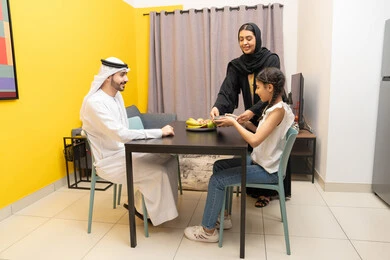 Fresh healthy fruits, sharing breakfast with family, eating a healthy meal, family breakfast, an Emirati Gulf Arab woman wearing a black abaya preparing a healthy snack for her daughter, kindness and tenderness between family members, a Gulf girl eating snacks