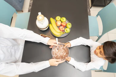 إفطار صباحي عائلي، تناول وجبة صحية، صورة مقربه ليد أب عربي خليجي إماراتي يجلس على الطاولة يقدم وعاء من حبوب الشوكولاتة بالحليب لابنه، اجواء عائلية سعيدة، العطف والحنان بين أفراد الأسرة