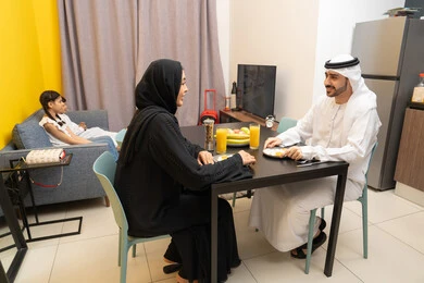 المحادثة والدردشات بين أفراد العائلة، تدعيم أواصر المحبه والترابط الأسري، عائله عربيه خليجيه اماراتية تجلس فى غرفه المعيشه داخل المنزل، رجل عربي خليجي اماراتي يرتدي الكندورة و الغتره يجلس على طاولة الطعام برفقه زوجته  يتناولون الافطار ،طفلان خليجيان يجلسان على الاريكه