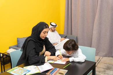 انشطة ترفيهية فنية ابداعية، مفهوم فنون الرسم عند الأطفال ، قضاء اوقات عائلية ممتعة ، أم عربيه خليجيه اماراتية ترتدي العباءة السوداء تجلس على الطاوله فى غرفه المعيشة تقوم بتعليم ومشاركة ابنها بالتلوين، حضانة أطفال ، التطوير والإبداع