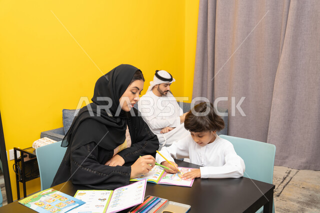ادوات ومعدات التلوين، مفهوم فنون الرسم عند الأطفال ، قضاء اوقات عائلية ممتعة ، أم عربيه خليجيه اماراتية ترتدي العباءة السوداء تجلس على الطاوله فى غرفه المعيشة تقوم بتعليم ومشاركة ابنها بالتلوين، حضانة أطفال ، التطوير والإبداع