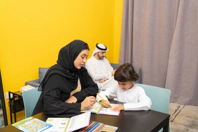 ادوات ومعدات التلوين، مفهوم فنون الرسم عند الأطفال ، قضاء اوقات عائلية ممتعة ، أم عربيه خليجيه اماراتية ترتدي العباءة السوداء تجلس على الطاوله فى غرفه المعيشة تقوم بتعليم ومشاركة ابنها بالتلوين، حضانة أطفال ، التطوير والإبداع