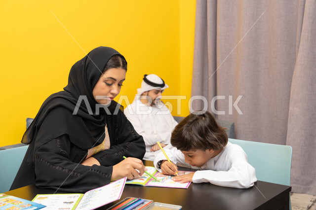 استخدام أقلام التلوين الخشبية، مفهوم فنون الرسم عند الأطفال ، قضاء اوقات عائلية ممتعة ، أم عربيه خليجيه اماراتية ترتدي العباءة السوداء تجلس على الطاوله فى غرفه المعيشة تقوم بتعليم ومشاركة ابنها بالتلوين، حضانة أطفال ، التطوير والإبداع