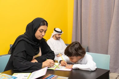 استخدام أقلام التلوين الخشبية، مفهوم فنون الرسم عند الأطفال ، قضاء اوقات عائلية ممتعة ، أم عربيه خليجيه اماراتية ترتدي العباءة السوداء تجلس على الطاوله فى غرفه المعيشة تقوم بتعليم ومشاركة ابنها بالتلوين، حضانة أطفال ، التطوير والإبداع