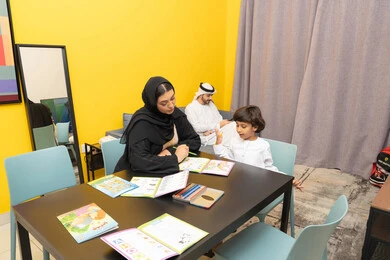 قضاء اوقات عائلية ممتعة، حل الواجبات المدرسية في المنزل، مفهوم فنون الرسم عند الأطفال، أم عربيه خليجيه اماراتية ترتدي العباءة السوداء تجلس على الطاوله فى غرفه المعيشة تقوم بتعليم ومشاركة ابنها بالتلوين، حضانة أطفال ، التطوير والإبداع