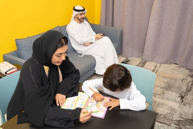 بناء علاقة متينة مع الأولاد، مفهوم فنون الرسم عند الأطفال ، قضاء اوقات عائلية ممتعة في المنزل،  ام عربيه خليجيه اماراتية ترتدي العباءة السوداء تجلس على الطاوله فى غرفه المعيشة تقوم بتعليم ومشاركة ابنها بالتلوين، حضانة أطفال ، التطوير والإبداع