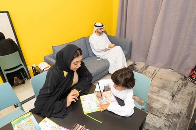 تنمية المهارات الفنية، مفهوم فنون الرسم عند الأطفال ، قضاء اوقات عائلية ممتعة في المنزل، ، ام عربيه خليجيه اماراتية ترتدي العباءة السوداء تجلس على الطاوله فى غرفه المعيشة تقوم بتعليم ومشاركة  ابنها بالتلوين، حضانة أطفال ، التطوير والإبداع