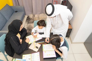 لعبة تلوين الرسومات، الاهتمام بتعليم بالأبناء ودعمهم، الانشطة التعليمية وتنمية القدرات، زوجان عربيان خليجيان اماراتيان يرتديان الزي التقليدي يجلسان على الطاولة يقومان بتعليم ابنائهم، استغلال أوقات الفراغ بالأنشطة الترفيهية الممتعة