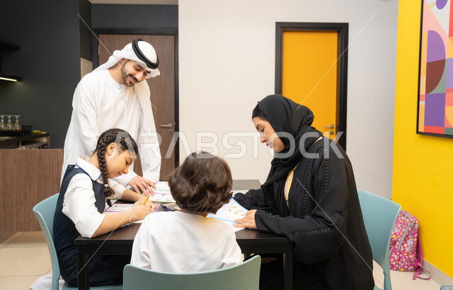 الاهتمام بتعليم بالأبناء ودعمهم، الانشطة التعليمية وتنمية القدرات، زوجان عربيان خليجيان اماراتيان يرتديان الزي التقليدي يجلسان على الطاولة يقومان بتعليم ابنائهم، استغلال أوقات الفراغ بالأنشطة الترفيهية الممتعة